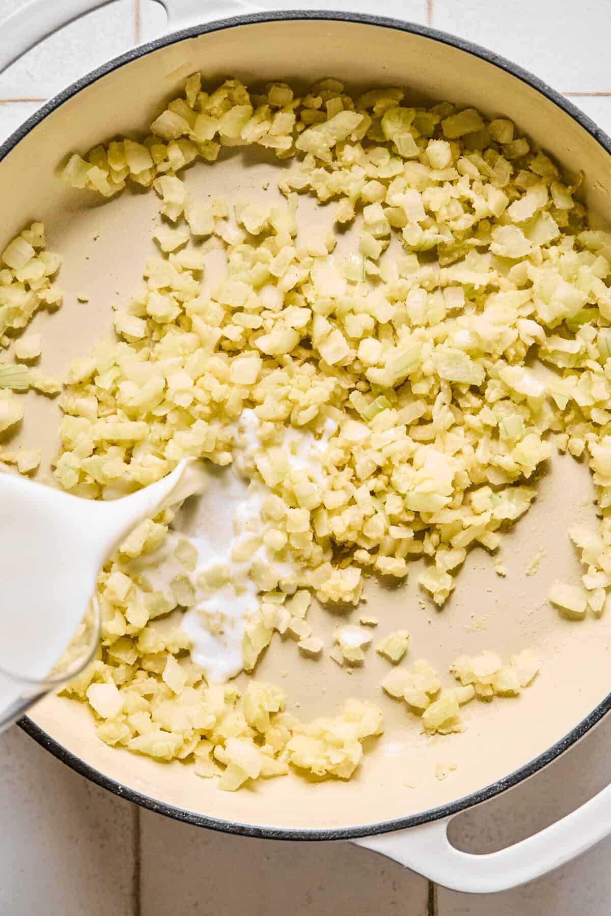Milk being poured into the pan with sautéed onions and garlic.