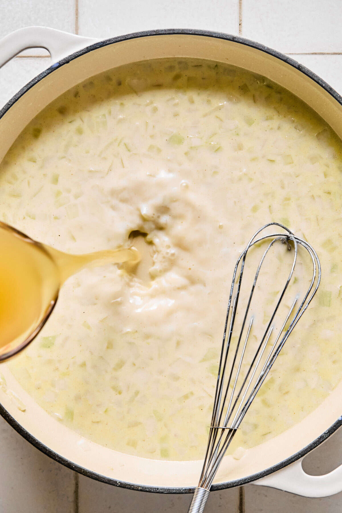 Broth being poured into the pan of milk, flour, and sautéed onions and garlic.