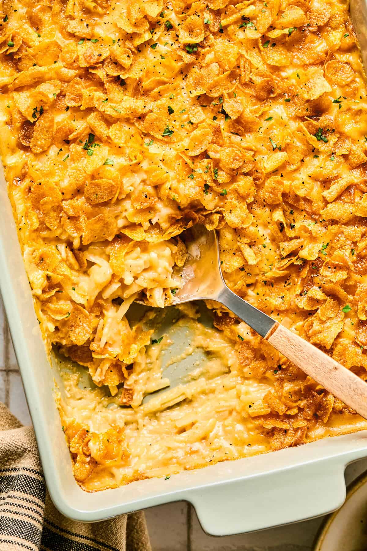 Cheesy hashbrown casserole in a large baking dish with a spoon scooping a portion out.