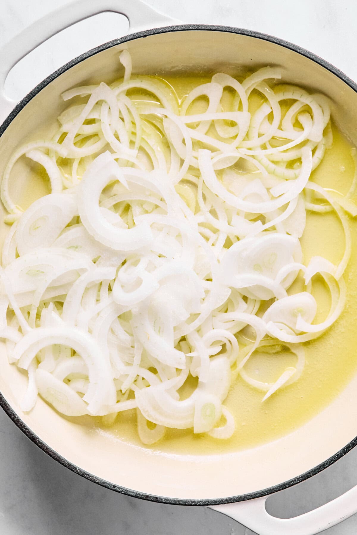 Large oven-safe skillet with melted butter and sliced onions.