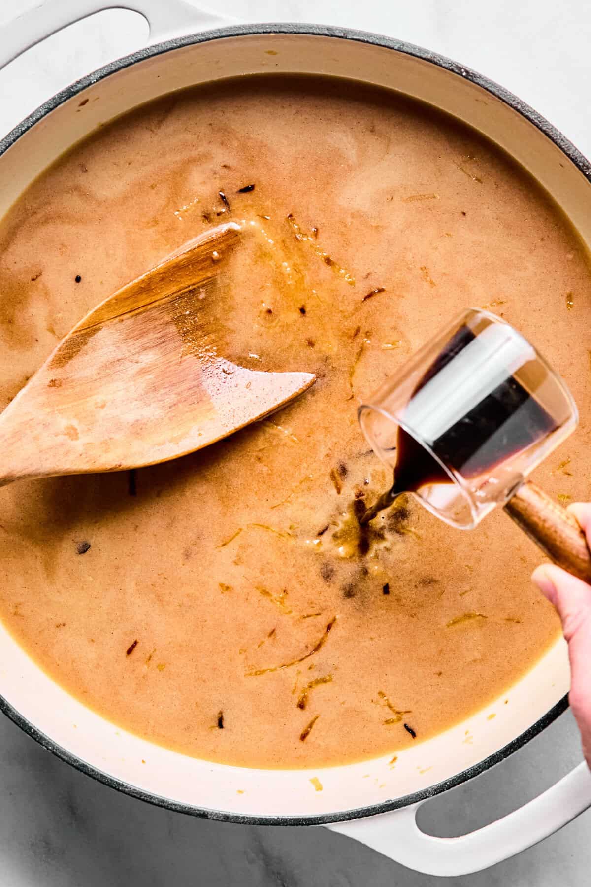 Beef broth, worcestershire sauce, thyme, and salt being poured into the oven-safe skillet over the caramelized onions.