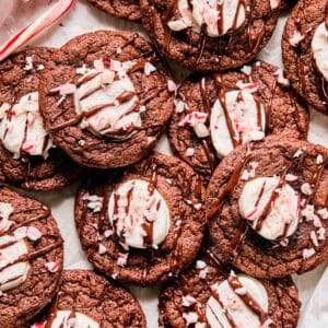 peppermint hot cocoa cookies with marshmallows in the middle topped with chocolate and crushed candy canes