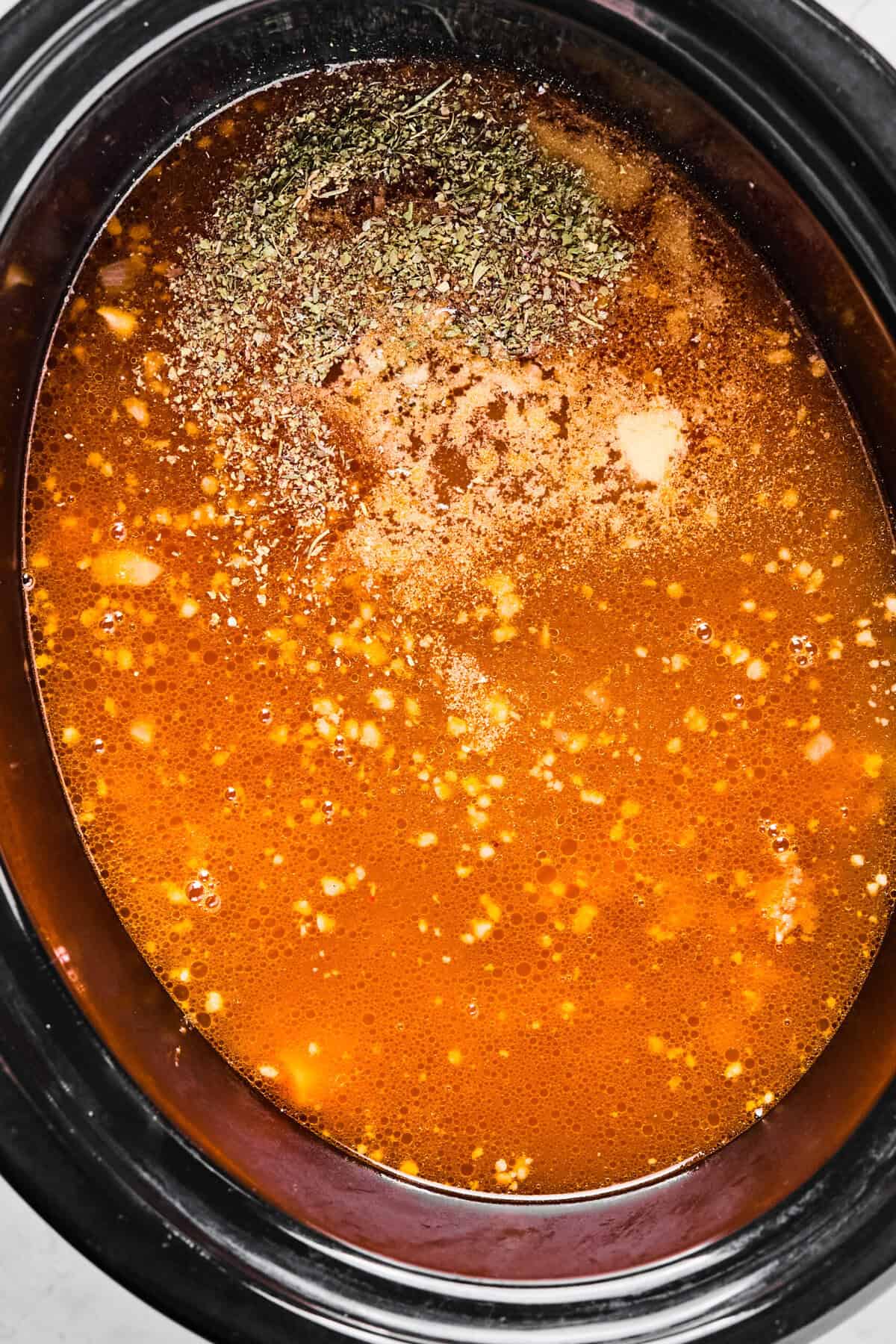 chicken broth and seasonings covering the sausage and veggies in the crockpot 
