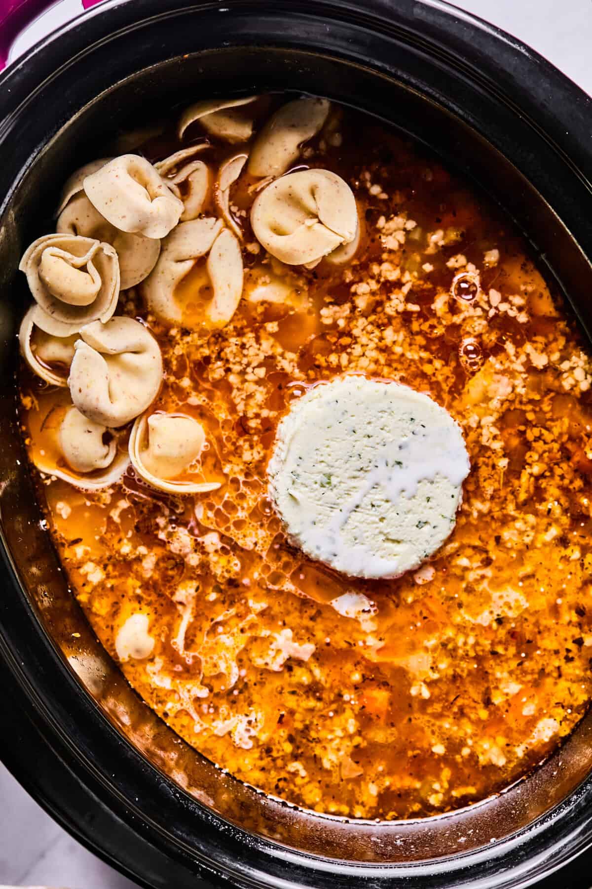 adding boursin cheese and tortellini to the crockpot 