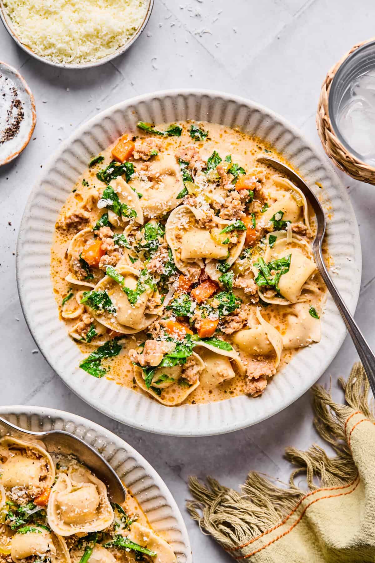 creamy sausage tortellini soup in a white bowl with spinach and veggies and a creamy boursin cheese sauce
