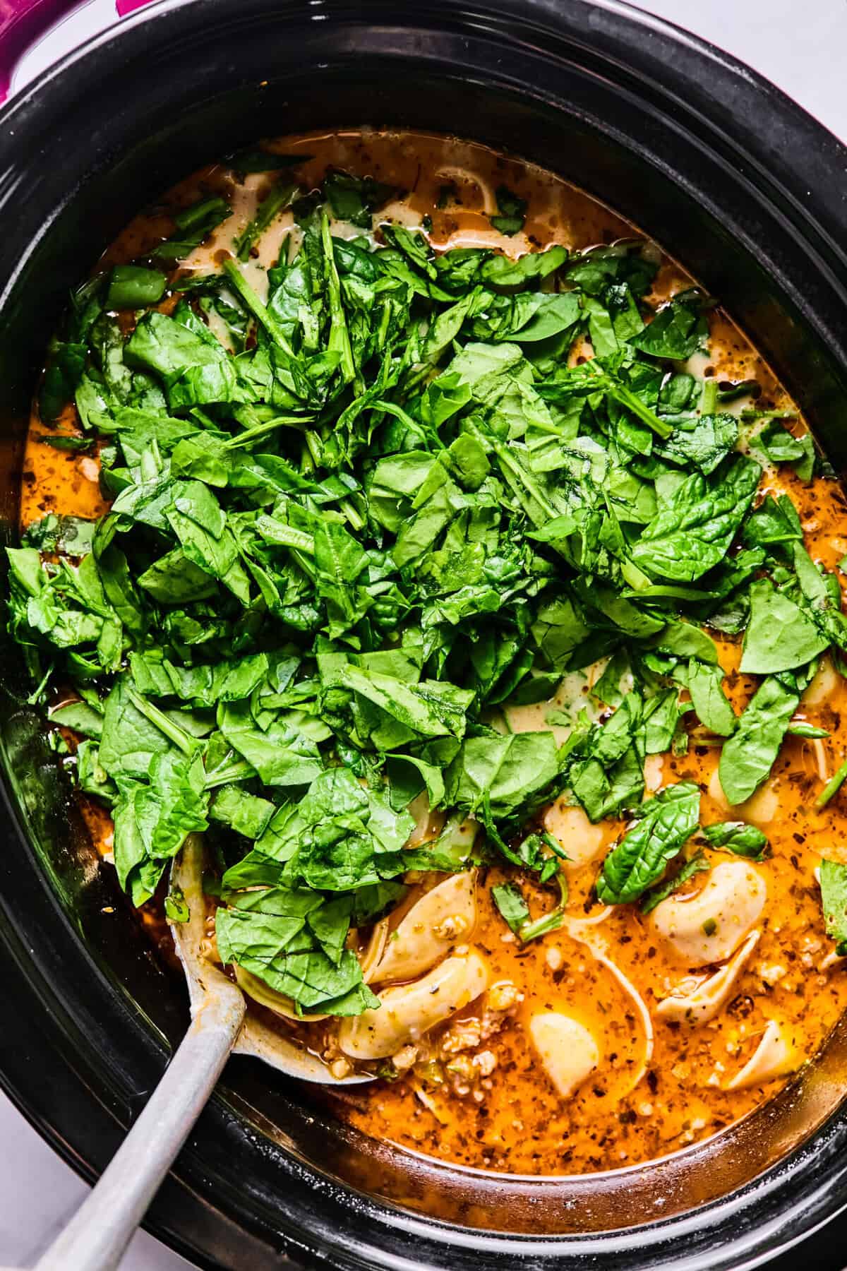 adding raw spinach to the crockpot soup. 