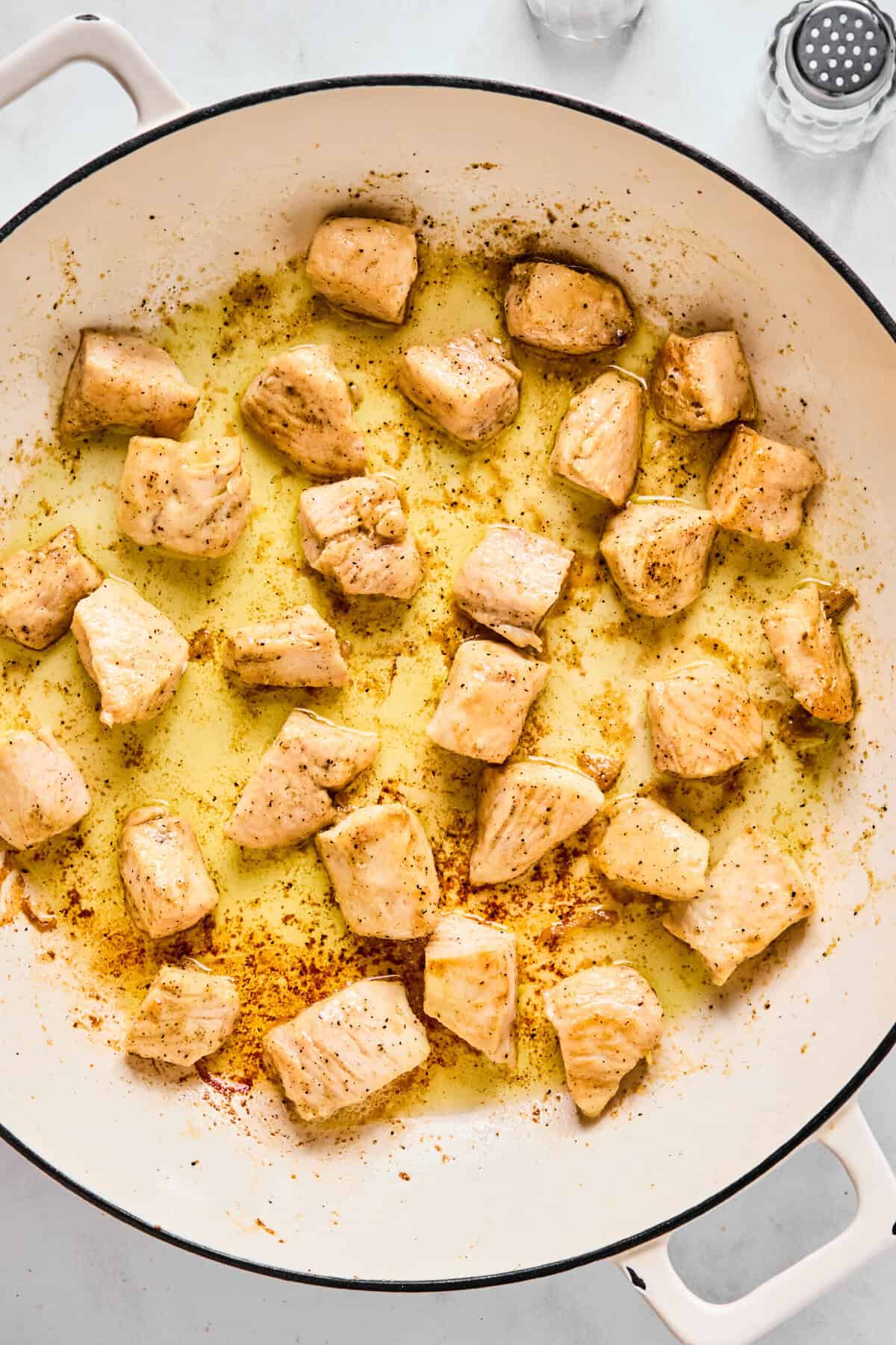 Chicken pieces browning in olive oil in a large sauté pan.
