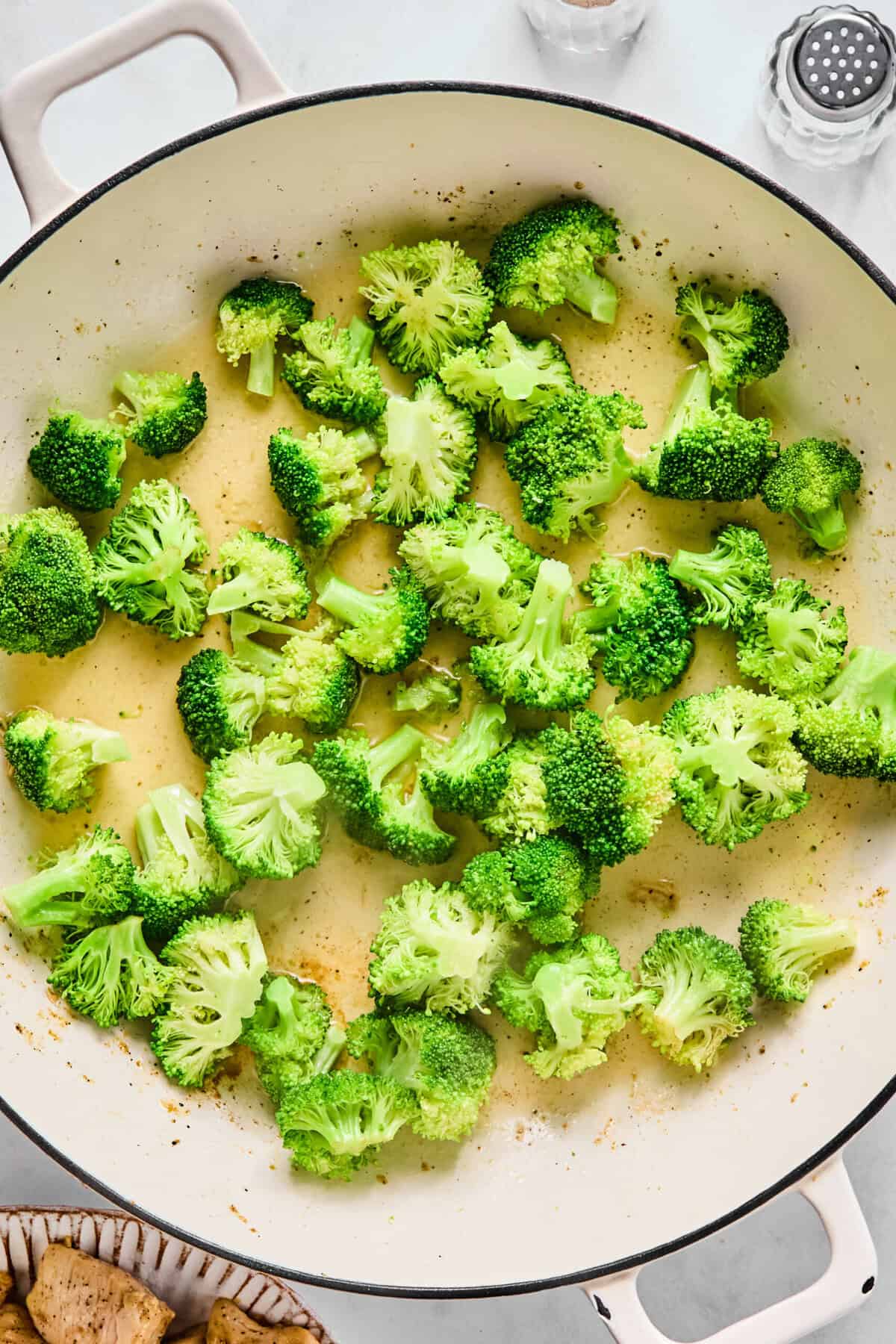 Broccoli florets steaming with a splash of water in a large sauté pan.