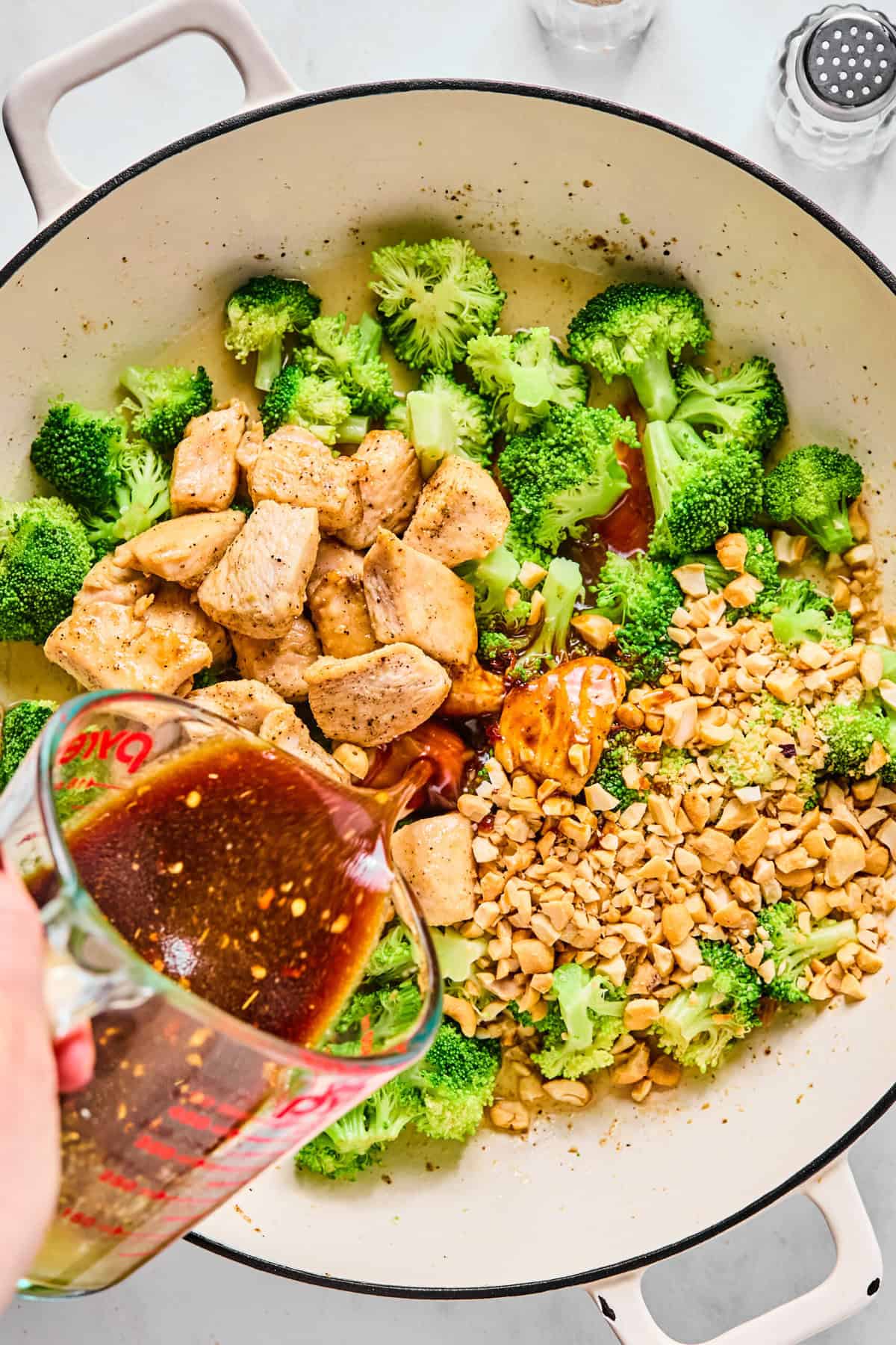 Chicken and cashews added back to large sauté pan with broccoli; stir fry sauce is being poured in.