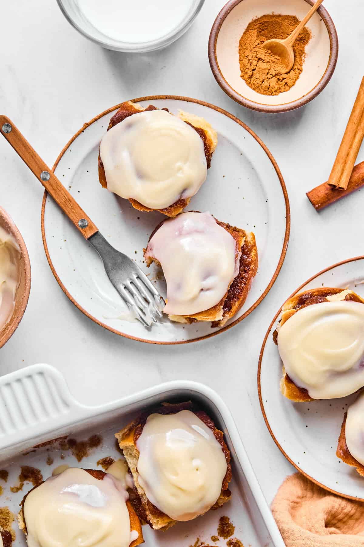 2 cinnamon rolls on a plate with a fork surrounded by more cinnamon rolls