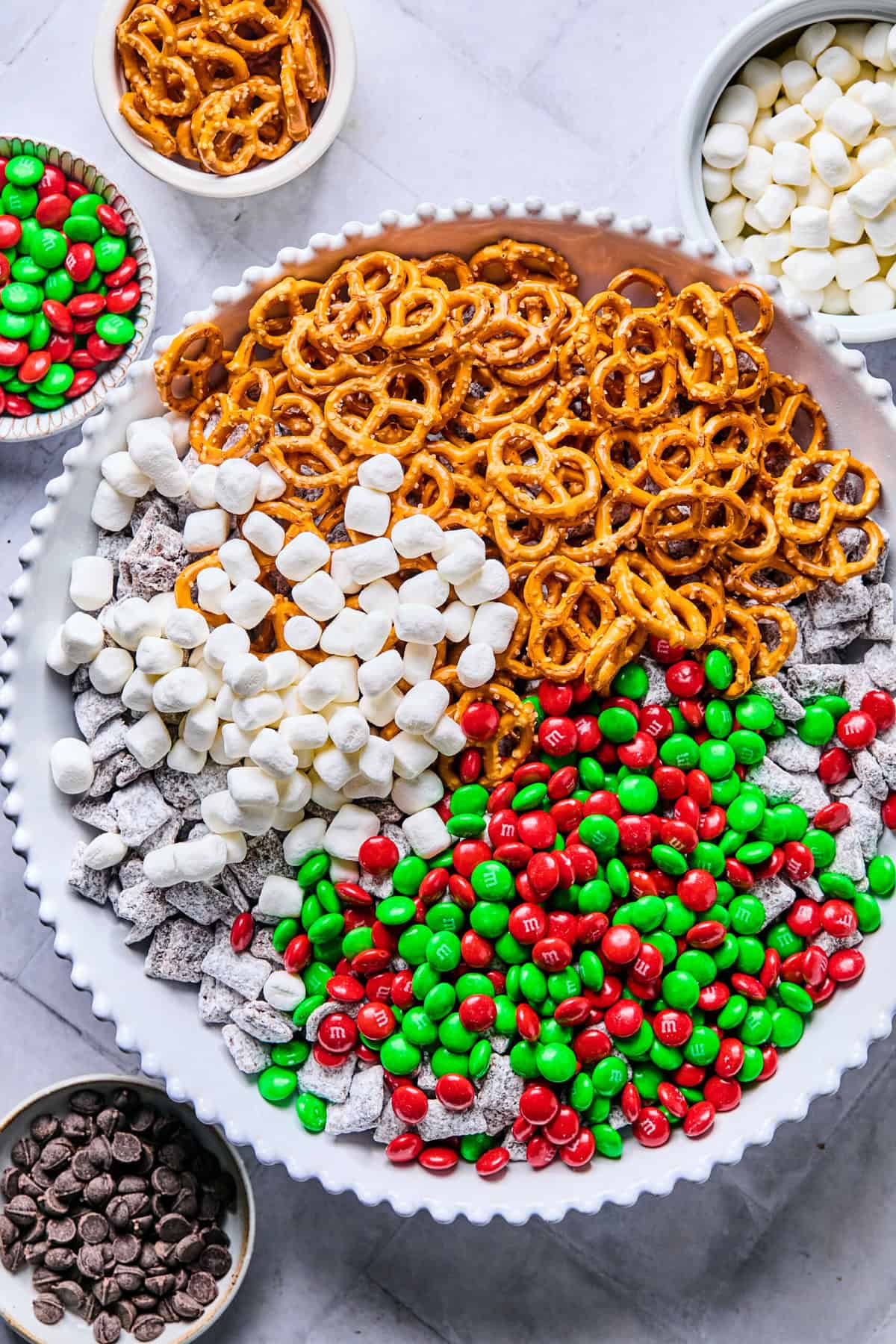 Cereal mixture in a clean bowl with gluten-free pretzels, Christmas M&Ms, and marshmallows; ready to combine.