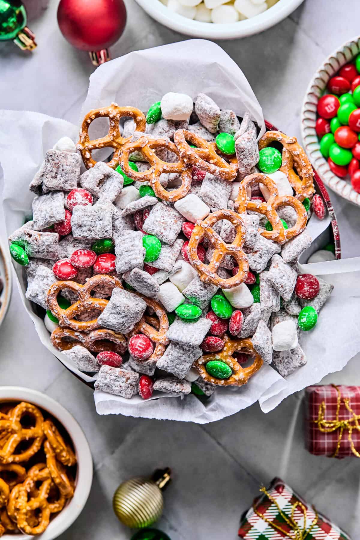 Overhead view of a festive parchment-lined serving tin filled with Christmas puppy chow on a white countertop.