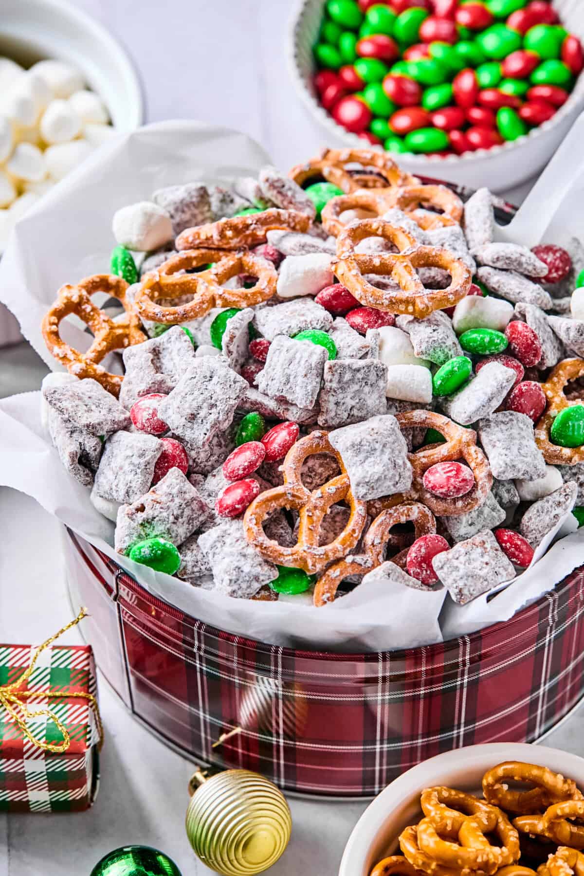 A festive parchment-lined tin filled with Christmas puppy chow on a white countertop.