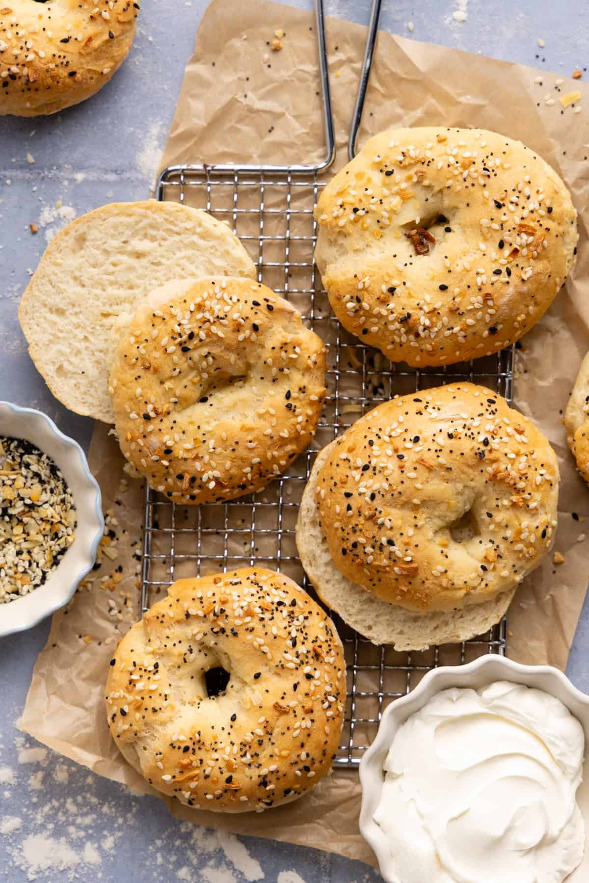Four cottage cheese bagels on a wire cooling rack with a small bowl of cream cheese next to it.
