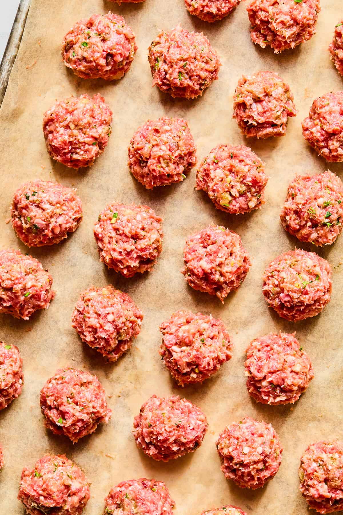 Greek lamb meatballs placed in even rows on a parchment-lined baking sheet.