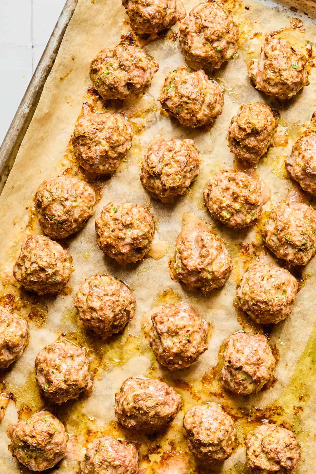 Lightly browned Greek lamb meatballs on a parchment-lined baking sheet.