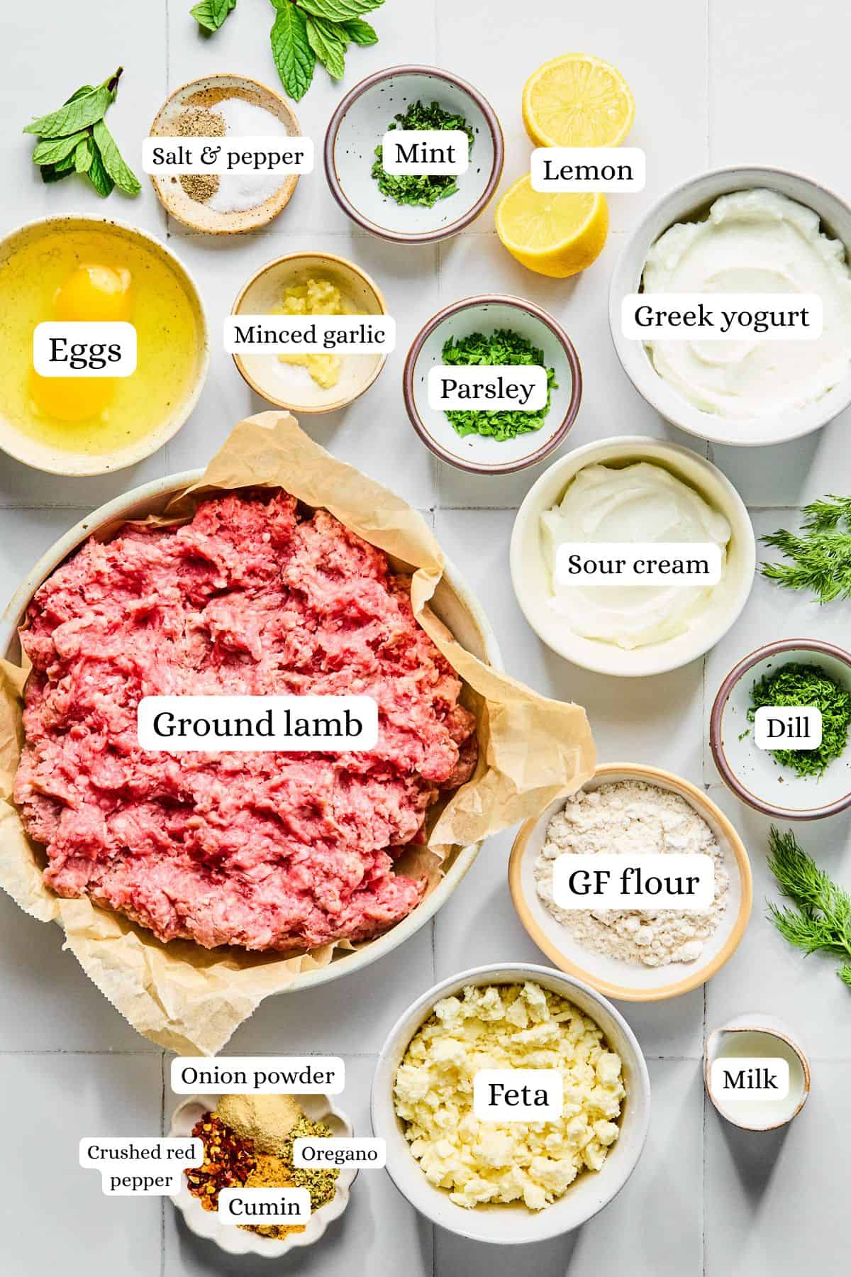 Greek lamb meatball ingredients laid out in nesting bowls on a white countertop.