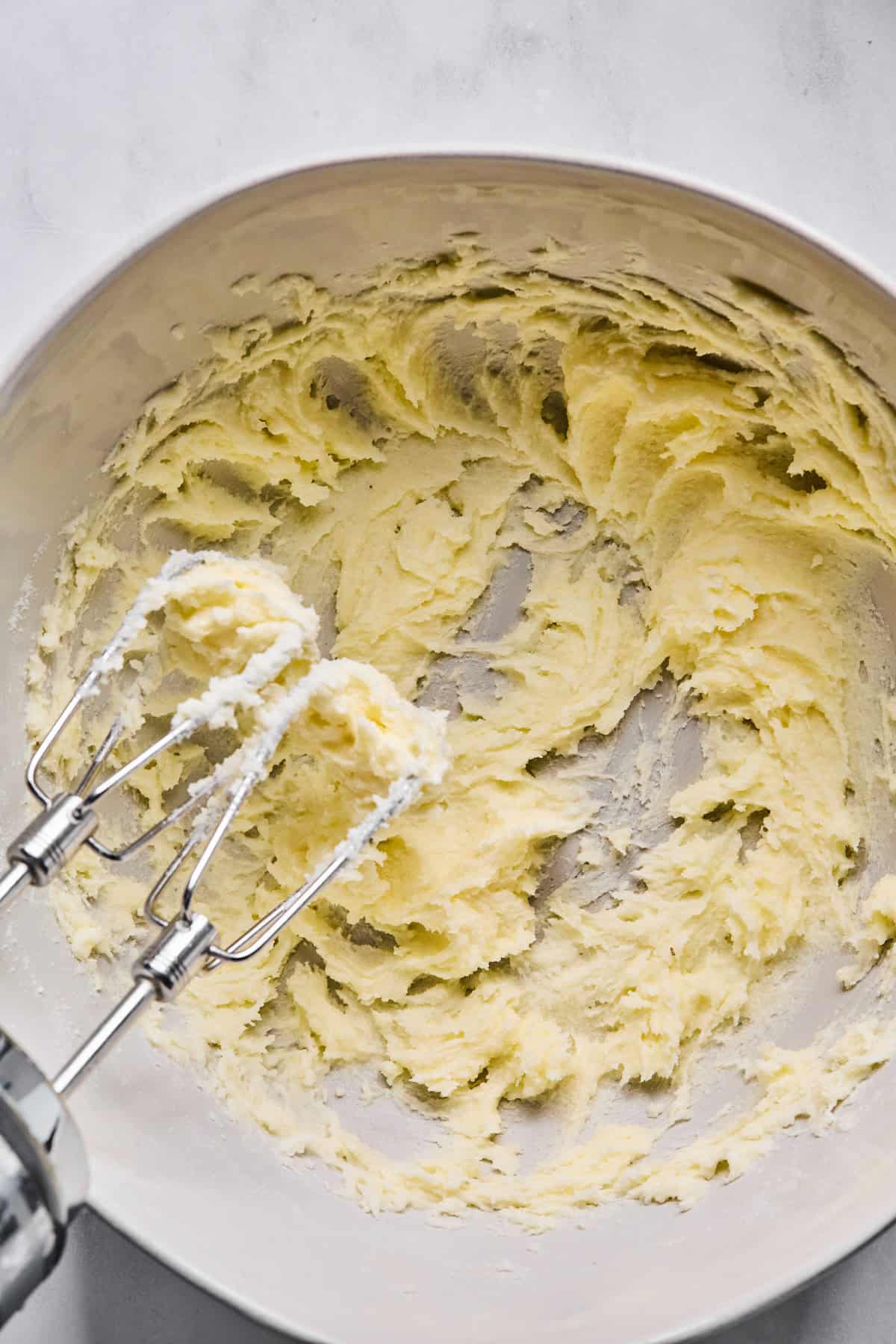 A large mixing bowl with softened butter and granulated sugar creamed together, with a handheld electric mixer resting on the bowl.