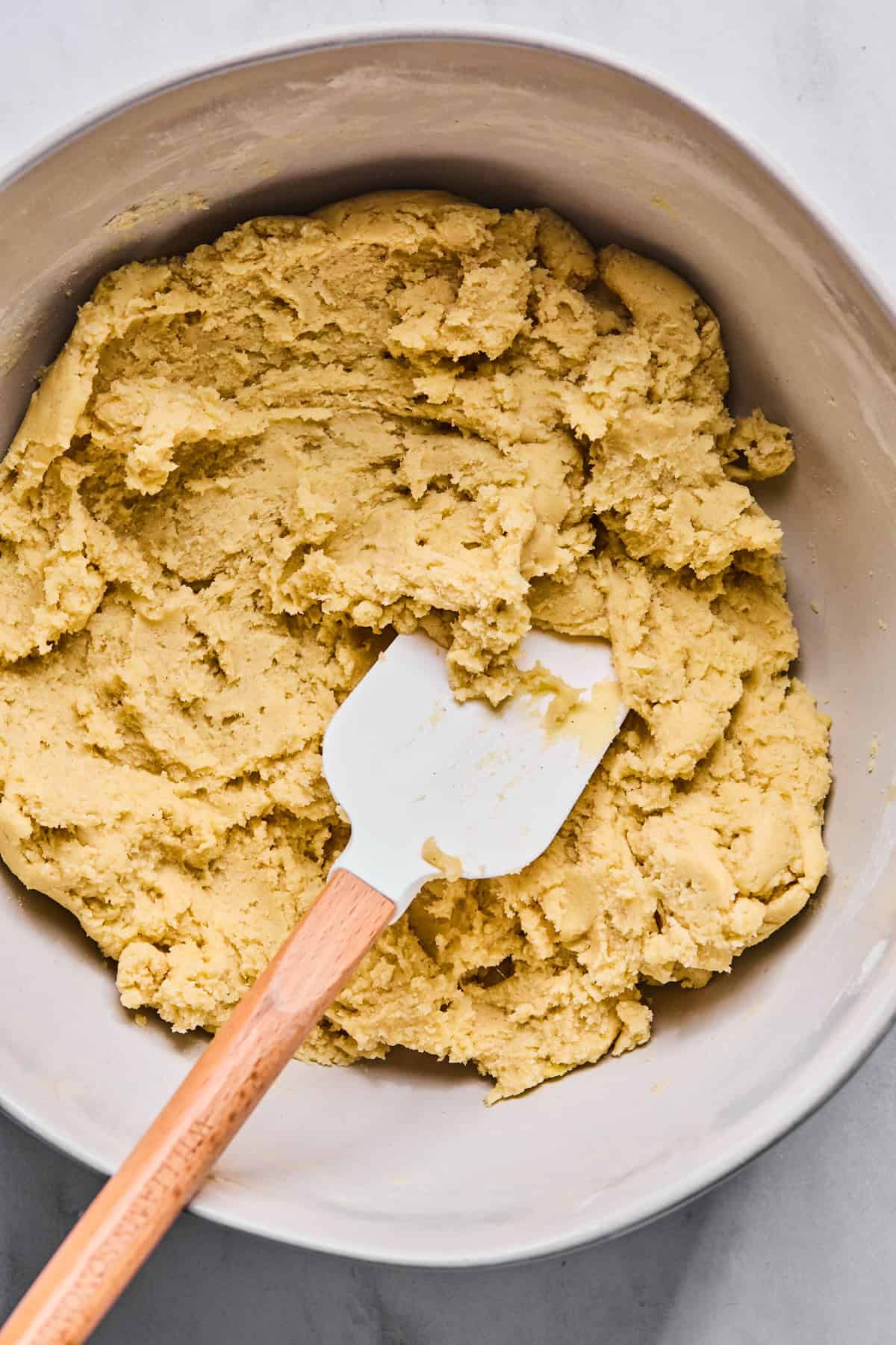 Gluten free Italian wedding cookie dough in a large bowl with a spatula resting in it.