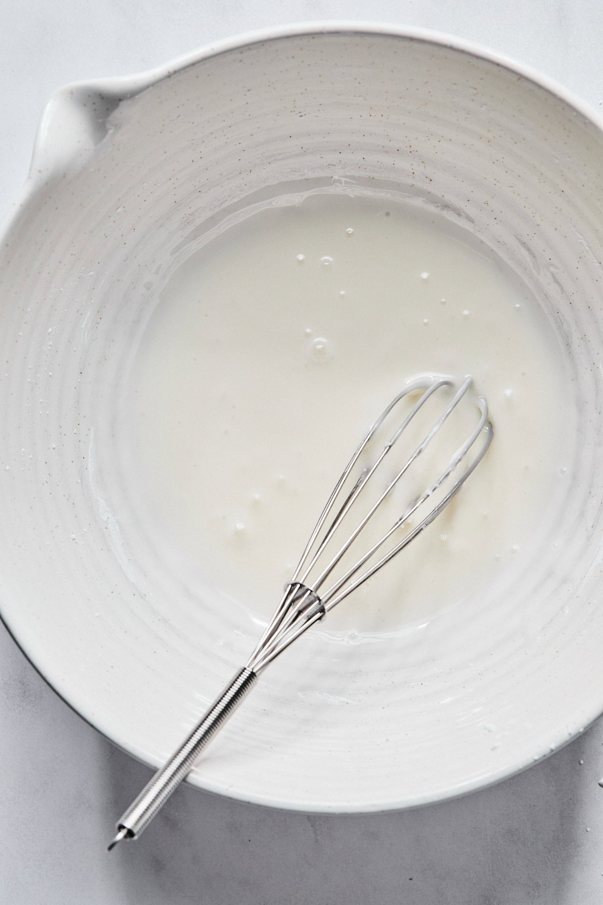 Almond glaze in a medium white bowl with a whisk resting in it.