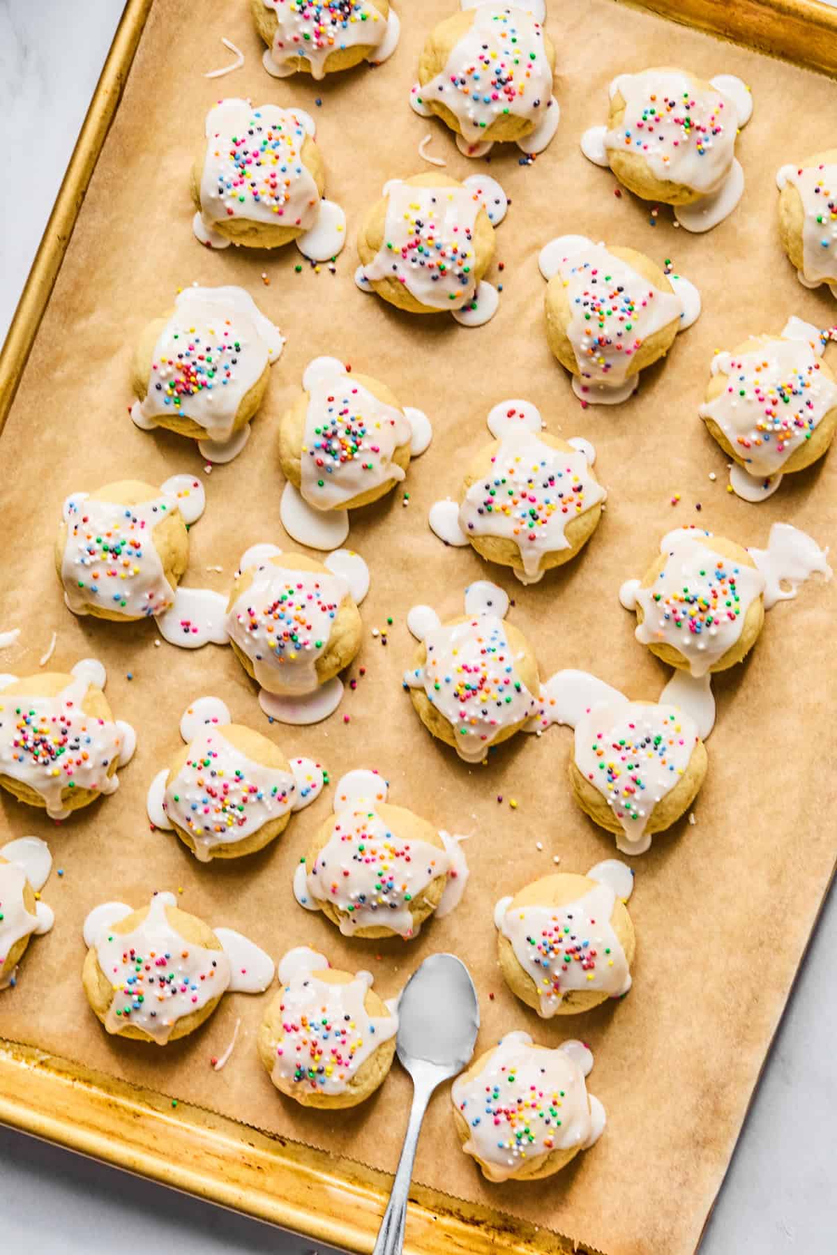 Gluten free Italian wedding cookies with almond glaze and rainbow sprinkles on a parchment lined baking sheet.