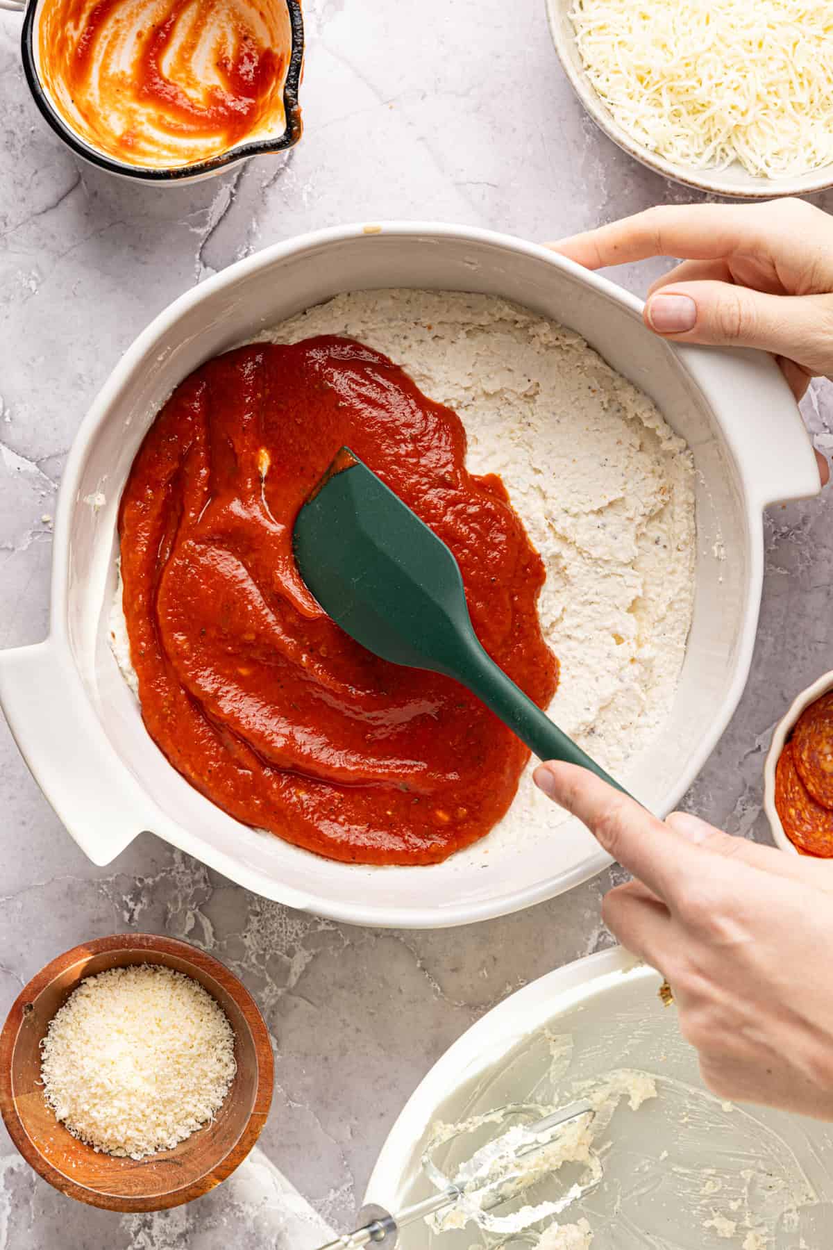 High protein pizza dip mixture spread out evenly in a dish; pizza sauce is being spread over it.
