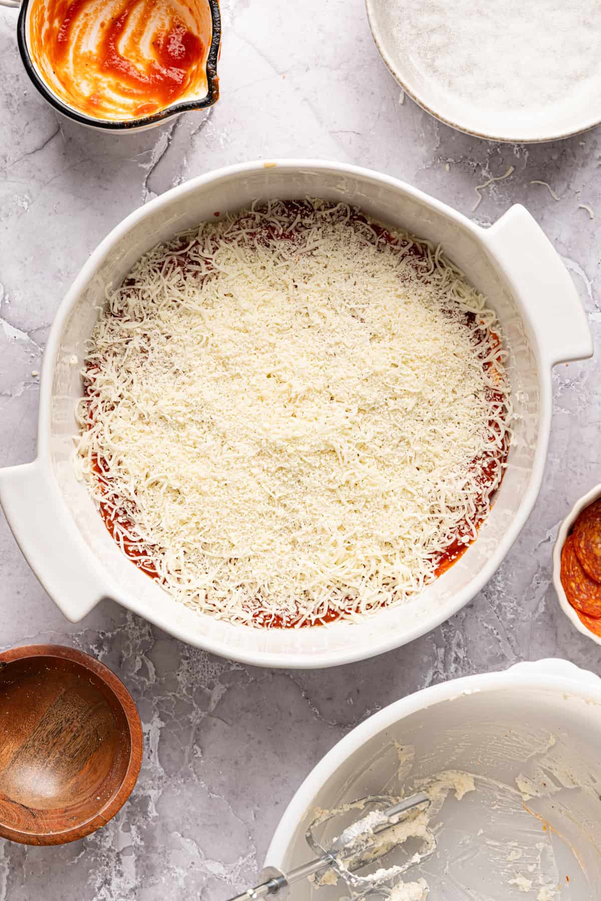 Shredded mozzarella and parmesan sprinkled over unbaked pizza dip with pizza sauce.