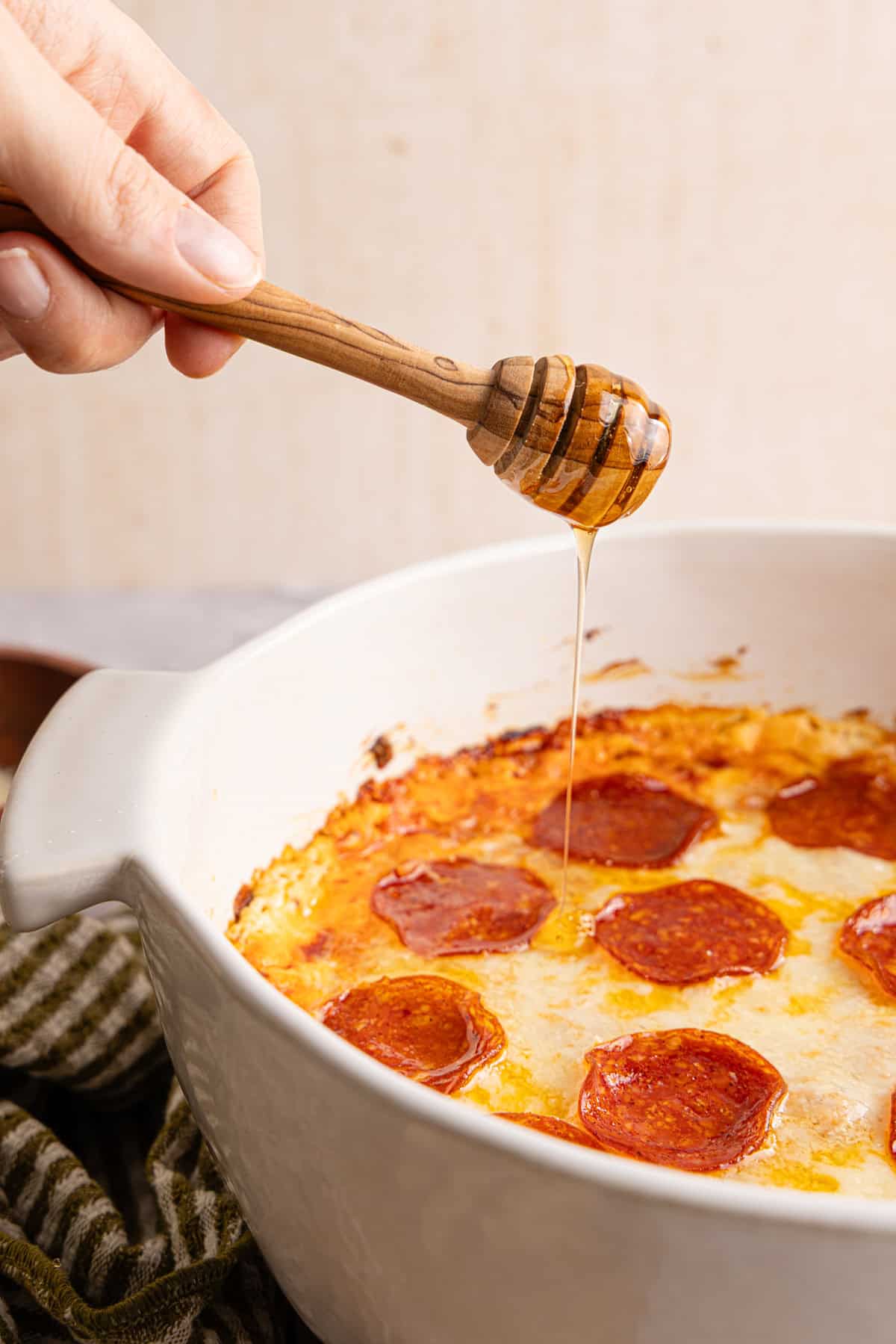 A hand drizzling hot honey over the baked high protein piza dip.