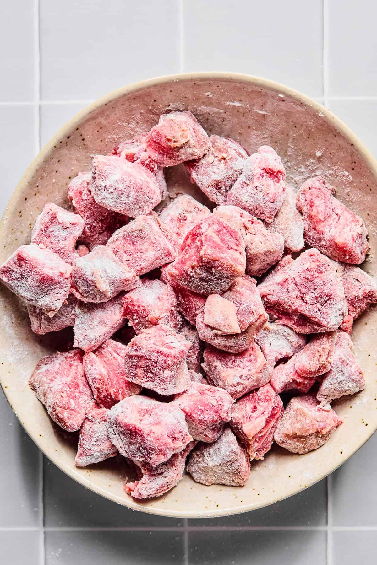 Stew meat in a bowl coated with gluten-free flour and salt and pepper.