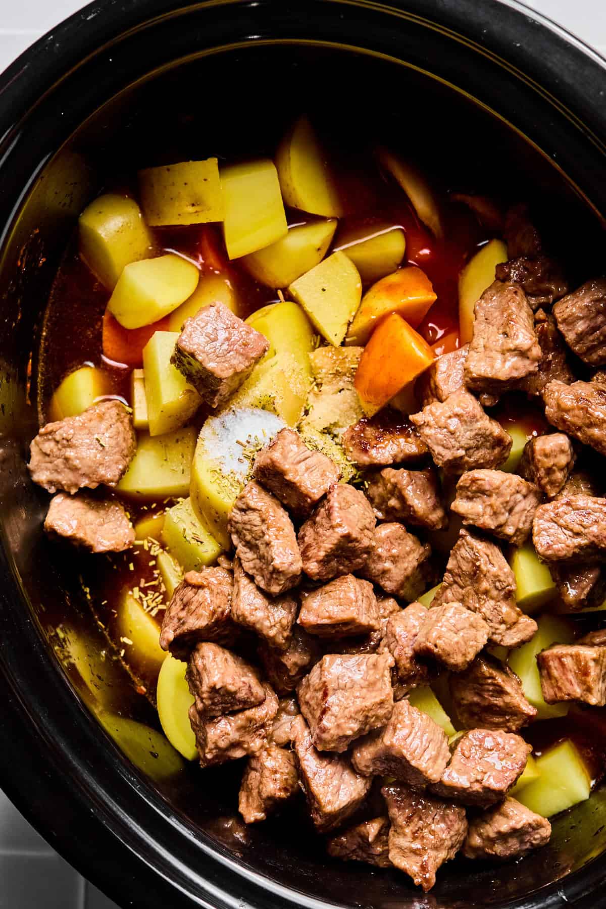 Stew meat, carrots, potatoes, Worcestershire sauce, hot sauce, rosemary, thyme, salt, and pepper in a slow cooker.