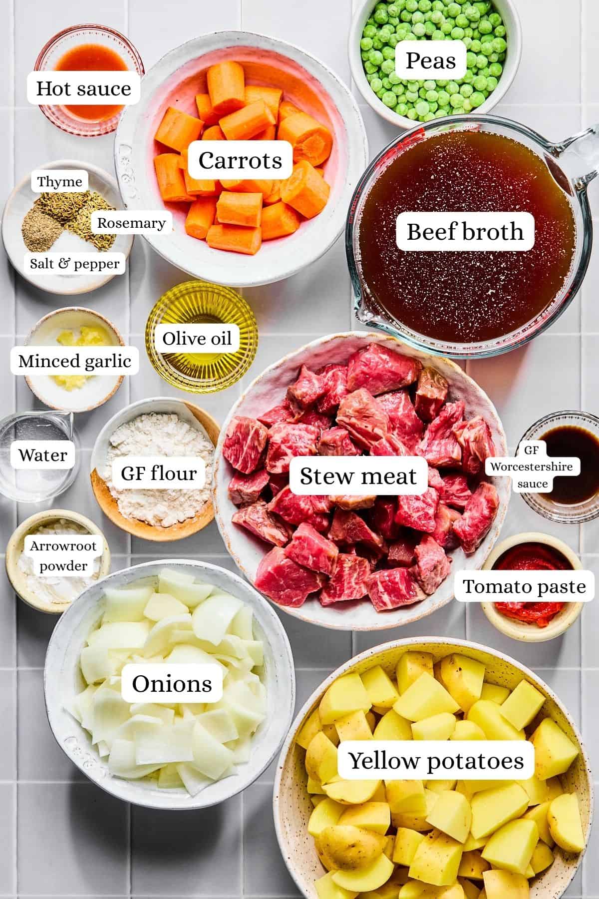 Slow cooker beef stew ingredients laid out in nesting bowls on a white countertop.