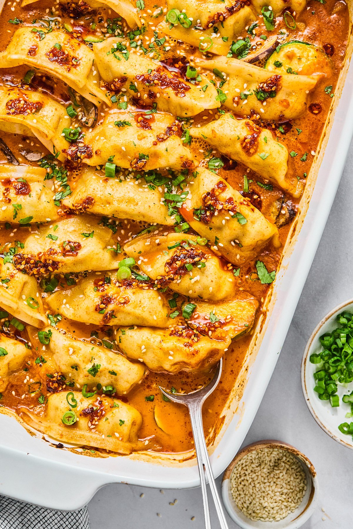 Gluten Free dumplings baked in a casserole dish with a red sauce topped with cilantro and green onions 