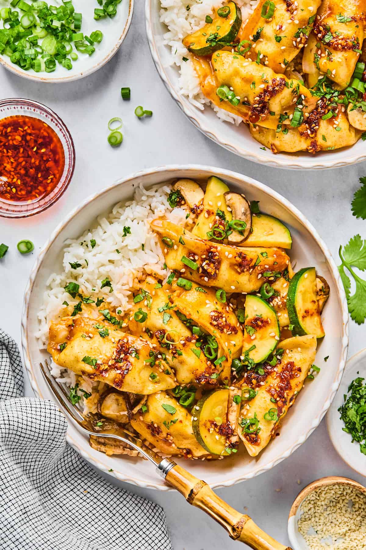 Gluten-free dumpling bake in two bowls served over white rice, topped with sliced green onions and sesame seeds.