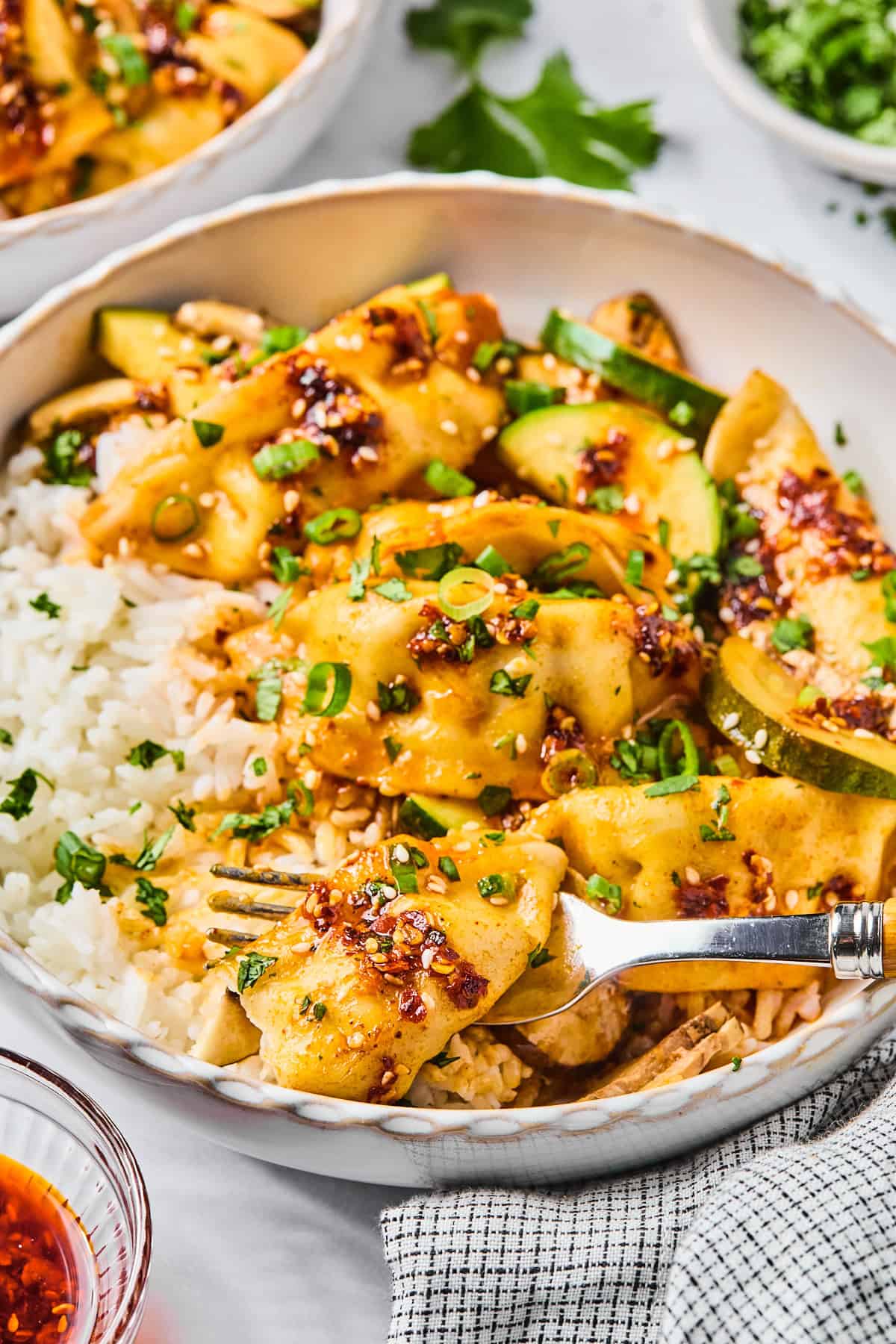Close-up of gluten-free dumpling bake served over white rice, topped with sliced green onions and sesame seeds, with a fork stuck into a dumpling