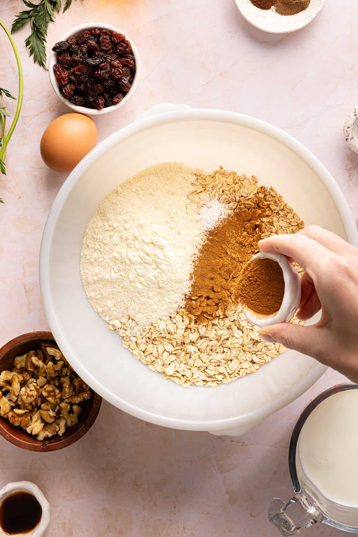 Dry ingredients including gluten-free oats, protein powder, and warm spices ready to be mixed together in a large bowl.