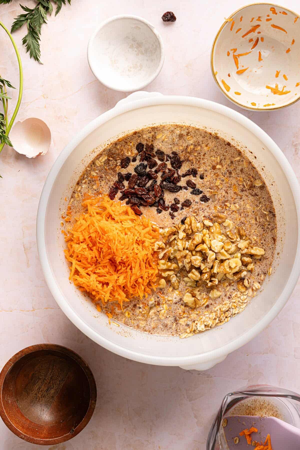 Finely shredded carrots, raisins, and chopped walnuts folded into carrot cake baked oats batter.