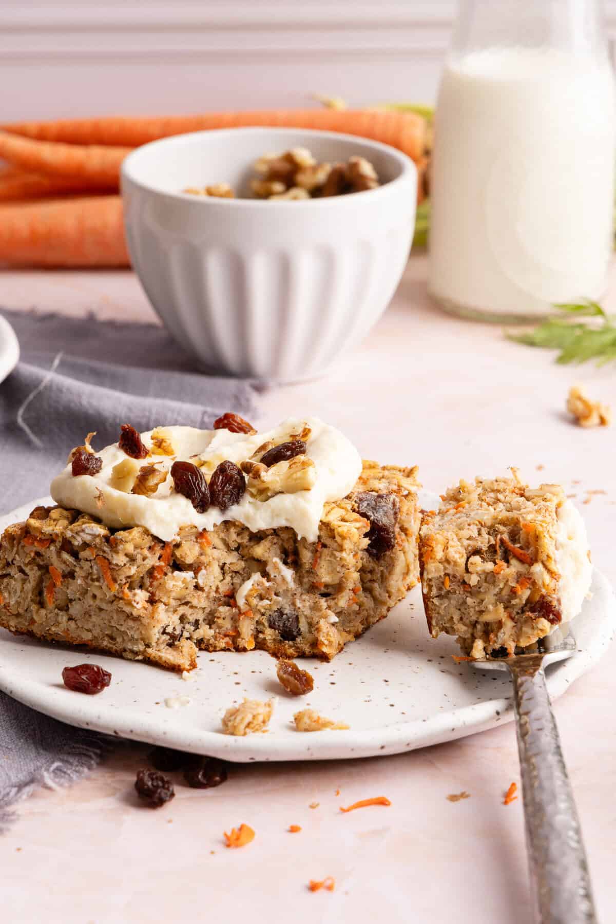 Close-up of carrot cake baked oats slice topped with protein cream cheese frosting, walnuts, and raisins.