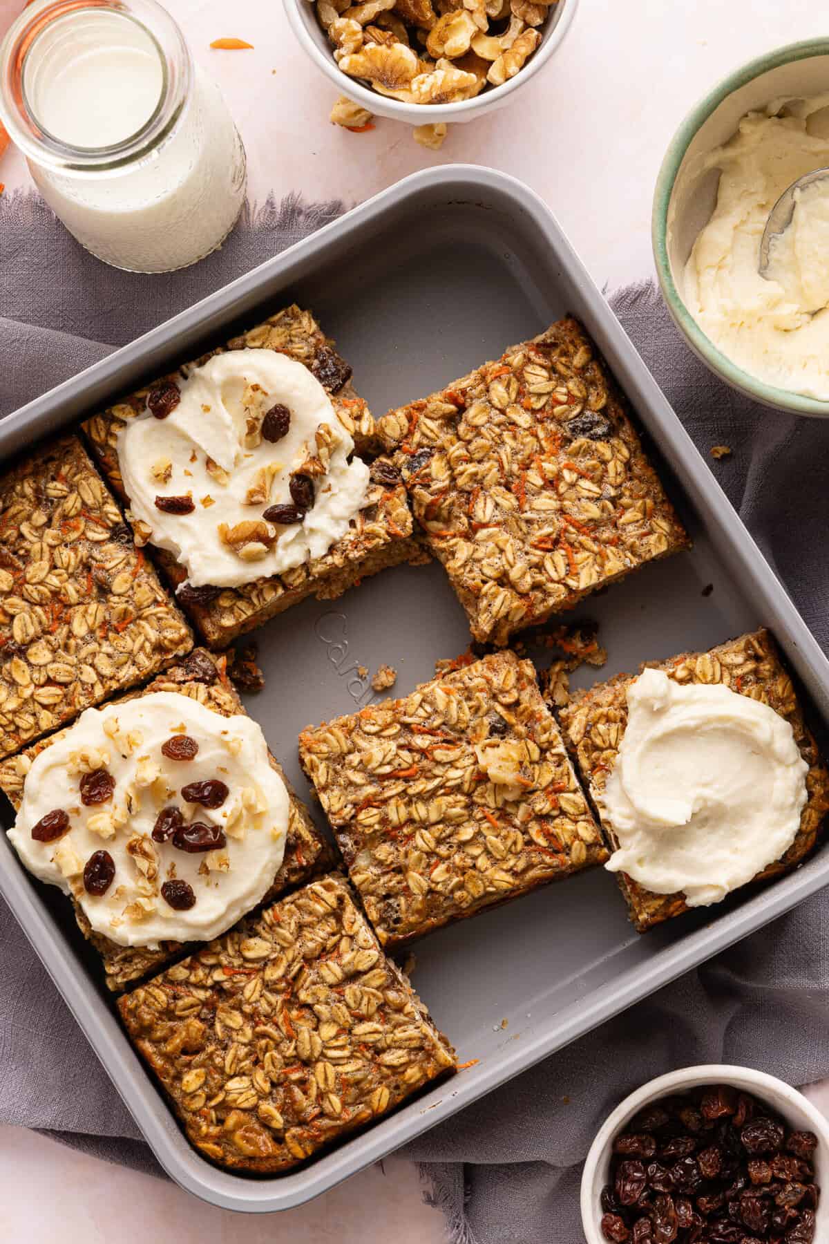 Sliced carrot cake baked oats; 3 of the slices have protein cream cheese frosting on them and are topped with raisins and walnuts.