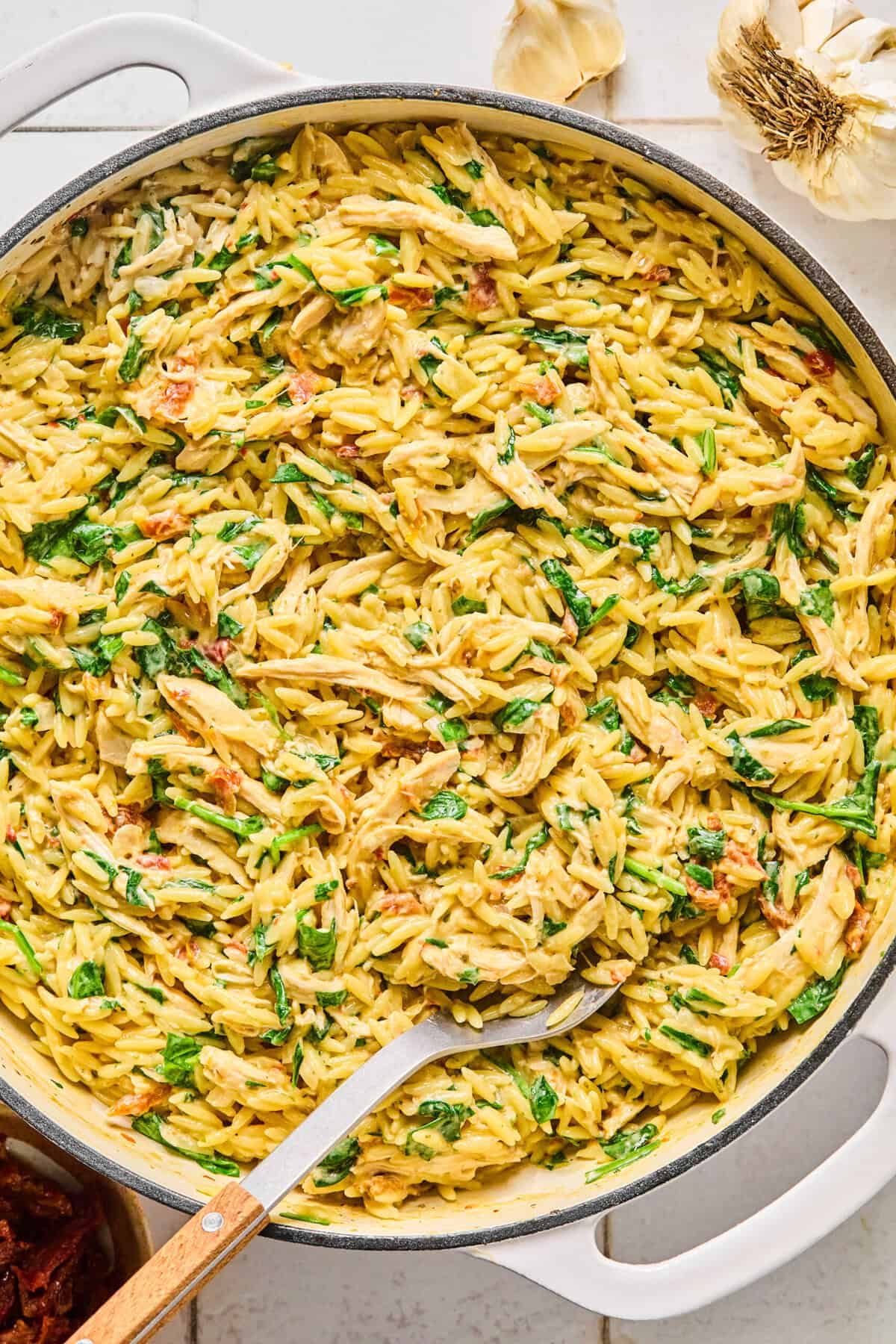 Marry me chicken orzo garnished with fresh basil and grated parmesan with a serving spoon resting in it.