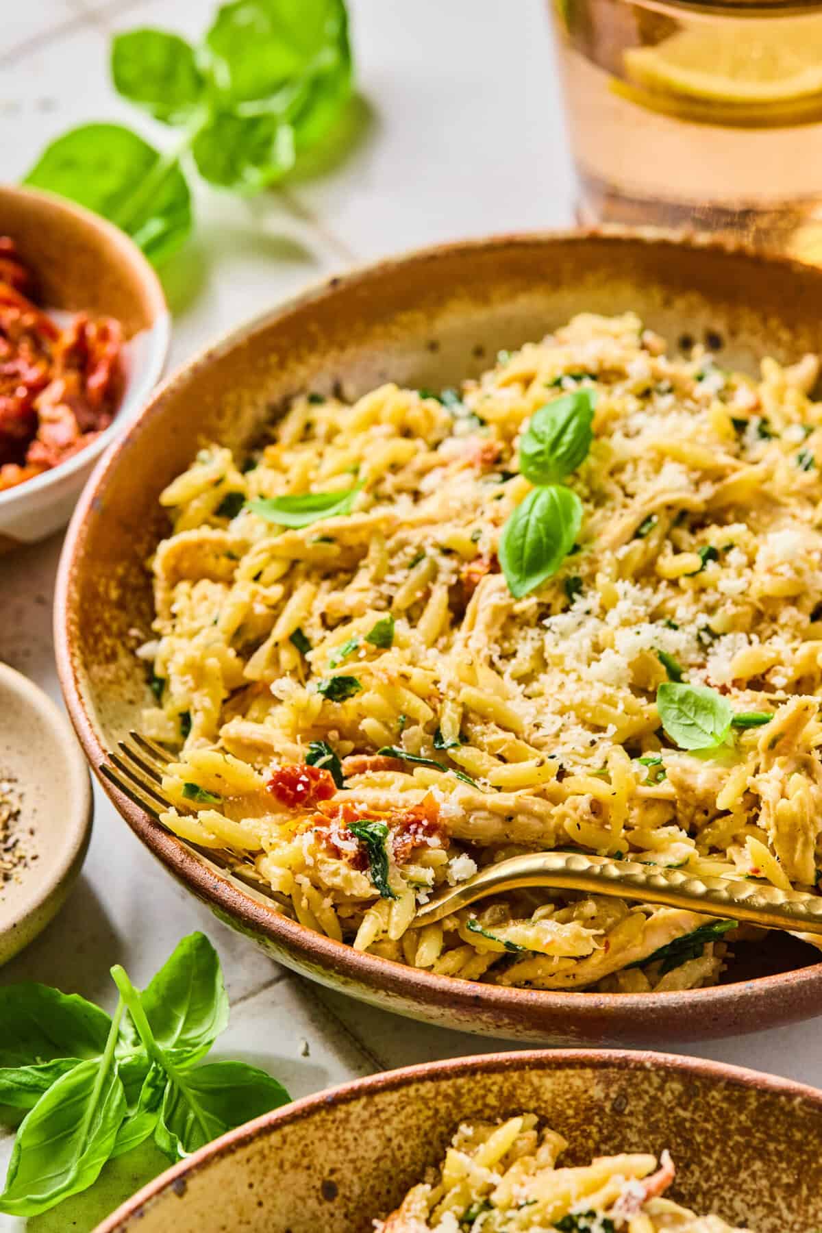 Marry me chicken orzo in a bowl with a fork lying in it. It’s garnished with fresh basil leaves.