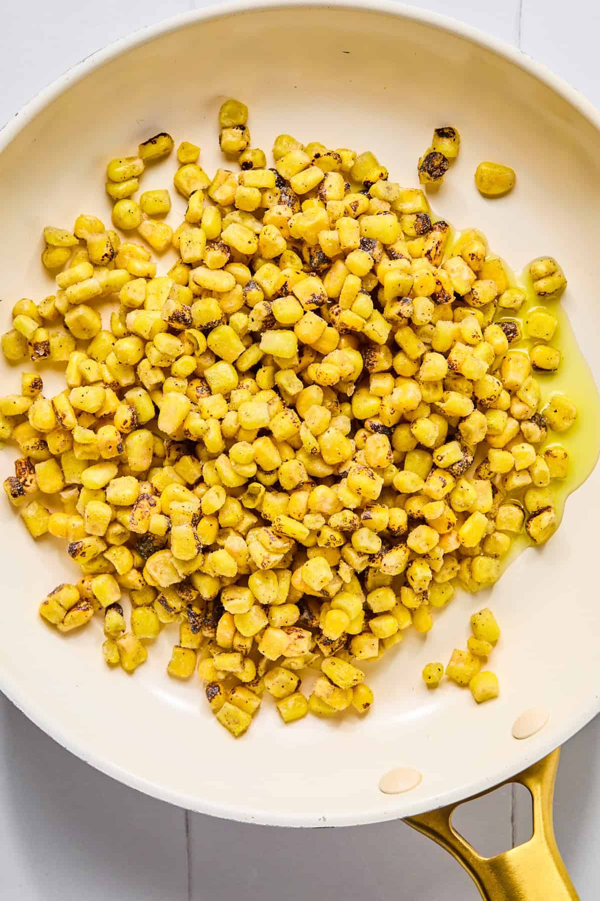 Charred corn cooking in a skillet in oil.