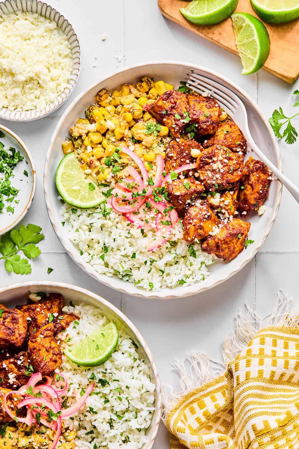Two street corn chicken rice bowls garnished with cilantro and a lime wedge, with a fork resting inside the main bowl.