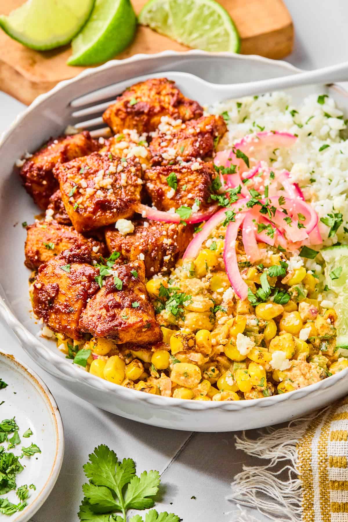 Close-up of a street corn chicken rice bowl with a fork lifting a piece of taco-seasoned chicken, garnished with fresh cilantro and lime.