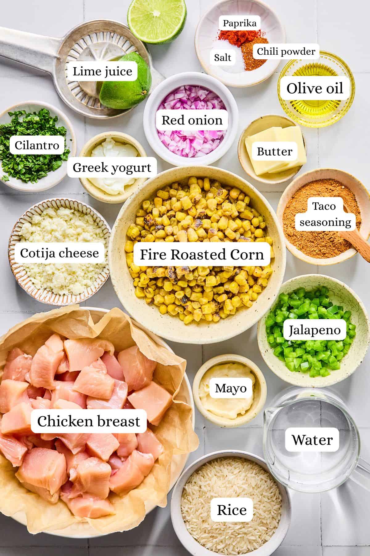 Ingredients for street corn chicken rice bowls labeled and arranged in small bowls on a white countertop.