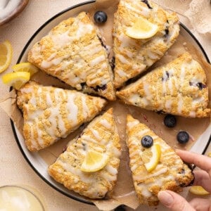 8 blueberry lemonade scones on a plate with lemon slices and a hand holding one