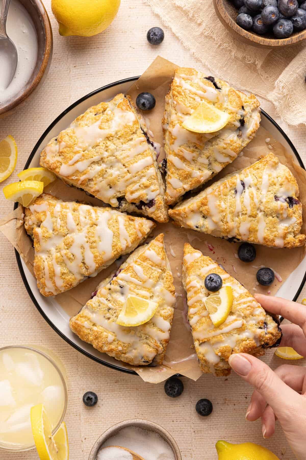8 blueberry lemonade scones on a plate with lemon slices and a hand holding one