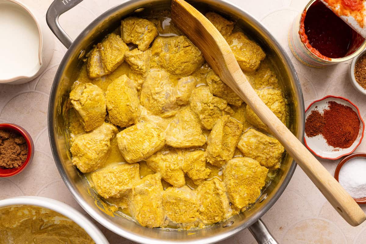 chicken cooking in a pan with a wooden spoon