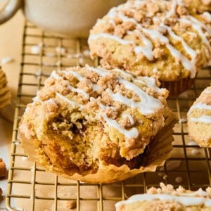 Coffee cake muffins on a cooling rack with one having a bite taken out of it