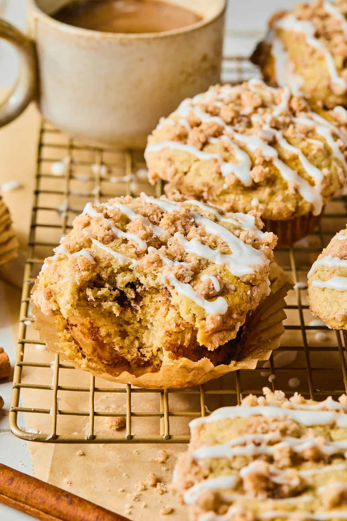 Coffee cake muffins on a cooling rack with one having a bite taken out of it
