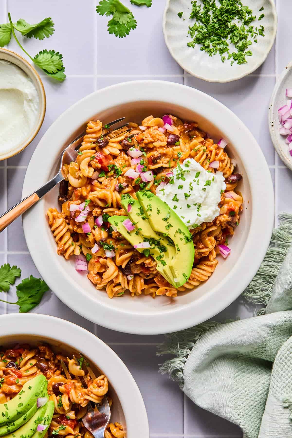 Bowl of one pot taco pasta garnished with sour cream, avocado, and cilantro with a fork.